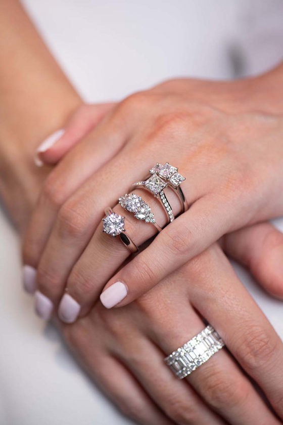 Womans hands with a range of sterling silver diamond engagement rings and diamond encrusted wedding band on other hand from Tom Coll Jewellery